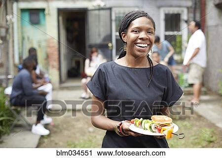 Stock Image - African American woman eating at backyard barbecue. Fotosearch