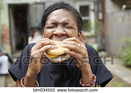 Stock Image - African American woman eating at backyard barbecue. Fotosearch