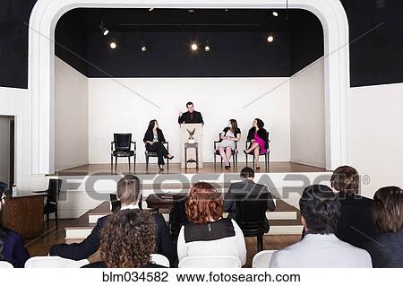 Stock Image - Audience listening to debate team speaking on stage. Fotosearch