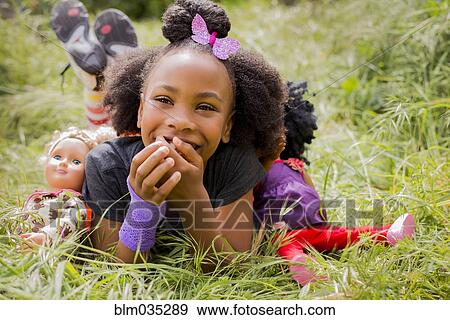 Stock Photo - Black girl playing with dolls in tall grass. Fotosearch