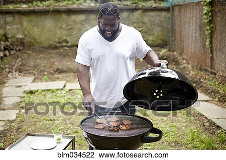 Stock Image - Black man grilling hamburgers at backyard barbecue. Fotosearch