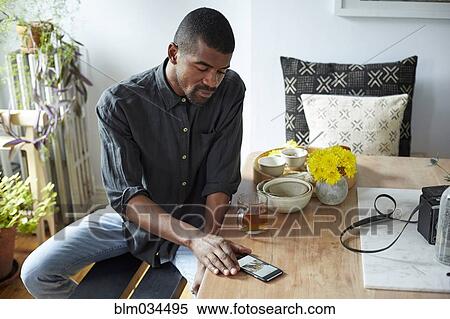 Stock Photography - Black man using cell phone at table. Fotosearch