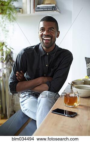 Picture - Black man with tea and cell phone at table. Fotosearch