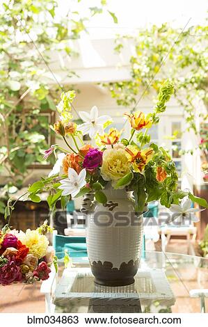 Stock Image - Bouquet of flowers in vase on backyard patio. Fotosearch
