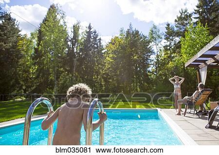 Stock Image - Boy climbing into swimming pool in backyard. Fotosearch