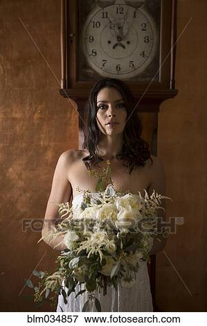 Stock Photo - Bride holding bouquet of flowers under grandfather clock. Fotosearch