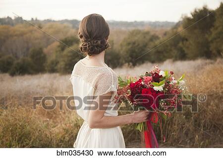 Stock Image - Bride holding bouquet on rural hilltop. Fotosearch