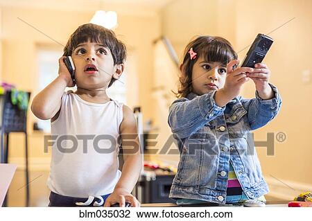 Stock Image - Brother and sister playing with cell phone and remote control. Fotosearch