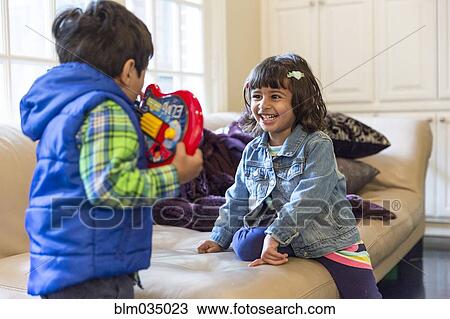 Stock Image - Brother and sister playing with toy in living room. Fotosearch