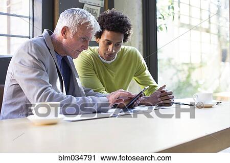 Stock Image - Business people using digital tablet in office meeting. Fotosearch