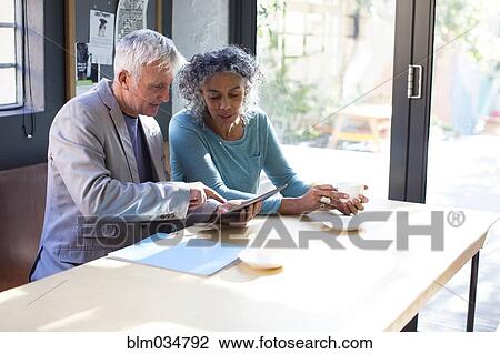 Stock Image - Business people using digital tablet in office meeting. Fotosearch