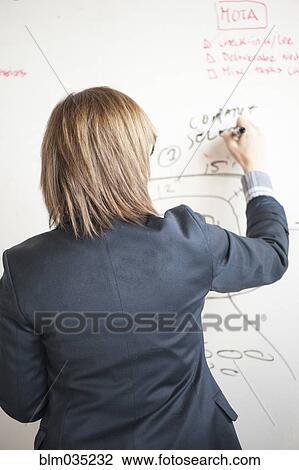 Stock Image - Businesswoman writing on whiteboard in office. Fotosearch