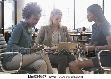 Stock Photo - Businesswomen using technology in office meeting. Fotosearch