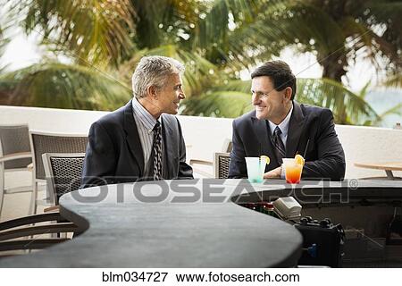 Stock Photo - Caucasian businessmen with cocktails at patio bar. Fotosearch