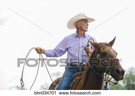 Stock Image - Caucasian cowboy riding horse in rodeo. Fotosearch