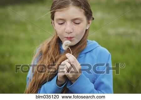 Stock Image - Caucasian girl blowing dandelion outdoors. Fotosearch