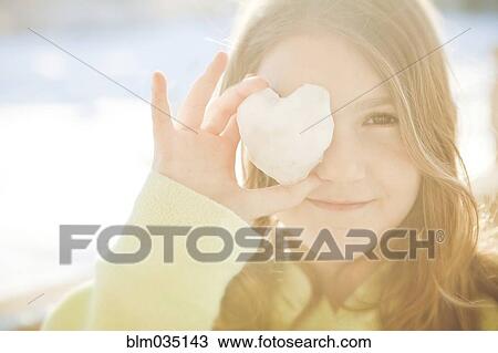 Stock Image - Caucasian girl covering eye with heart shape. Fotosearch