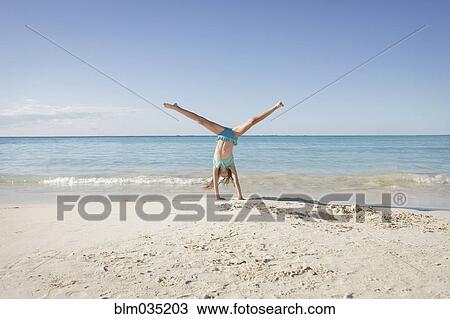 Stock Image - Caucasian girl doing cartwheel on beach. Fotosearch