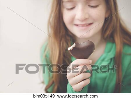 Stock Photo - Caucasian girl eating heart-shaped chocolate. Fotosearch