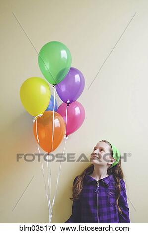 Stock Image - Caucasian girl holding bunch of balloons. Fotosearch