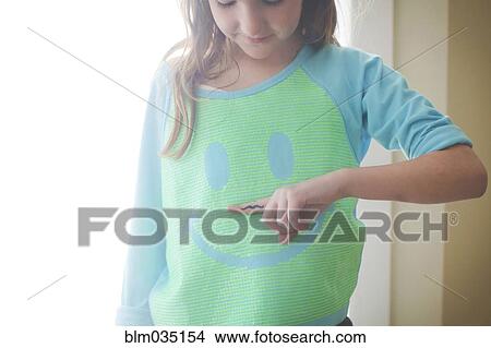 Picture - Caucasian girl holding mustache over smiley face shirt. Fotosearch