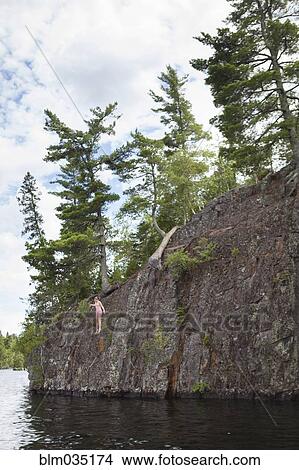 Picture - Caucasian girl jumping into lake from cliff. Fotosearch