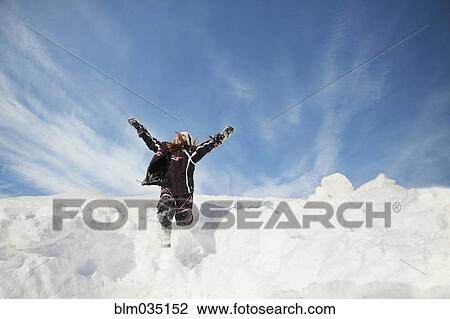 Stock Image - Caucasian girl jumping on snowy hillside. Fotosearch
