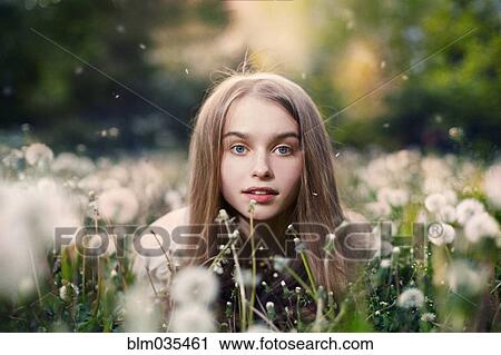 Stock Image - Caucasian girl laying in tall grass and dandelions. Fotosearch