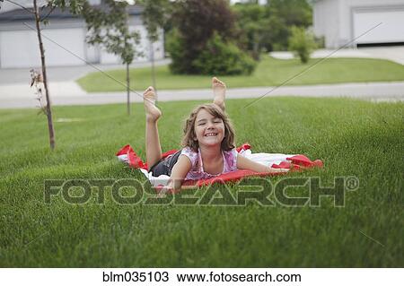 Stock Image - Caucasian girl laying on lawn in suburban neighborhood. Fotosearch