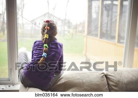 Picture - Caucasian girl looking out living room window. Fotosearch