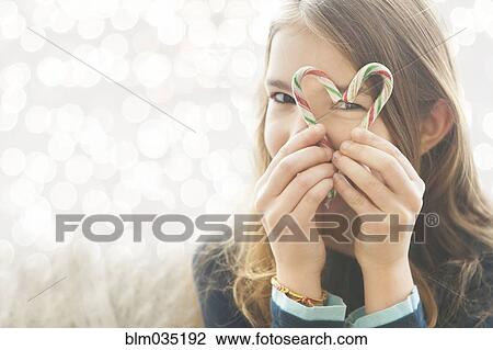 Stock Image - Caucasian girl looking through heart-shape with candy canes. Fotosearch