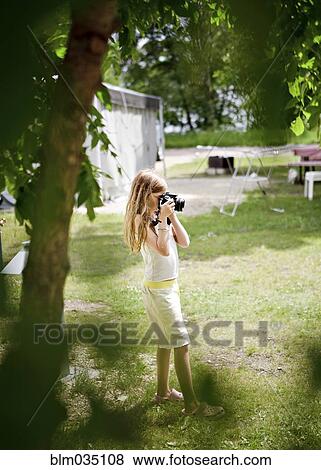 Stock Photo - Caucasian girl photographing in backyard. Fotosearch