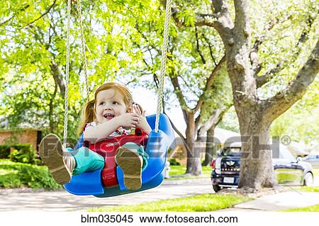 Stock Photography - Caucasian girl playing on swing in front yard. Fotosearch