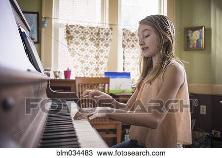 Stock Image - Caucasian girl playing piano in living room. Fotosearch