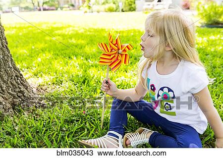 Stock Image - Caucasian girl playing with pinwheel in backyard. Fotosearch