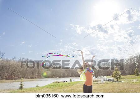 Stock Image - Caucasian girl playing with ribbons in park. Fotosearch