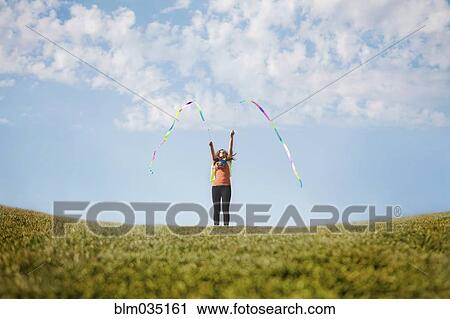 Stock Image - Caucasian girl playing with ribbons on hilltop. Fotosearch