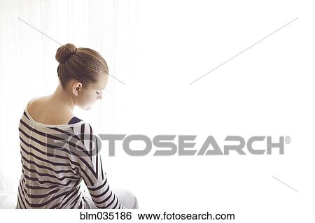 Stock Photograph - Caucasian girl sitting at sheer curtains. Fotosearch