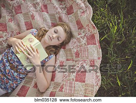 Stock Photo - Caucasian girl sleeping with book on blanket. Fotosearch