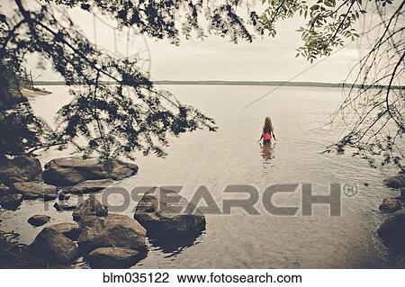 Stock Image - Caucasian girl standing in remote lake. Fotosearch