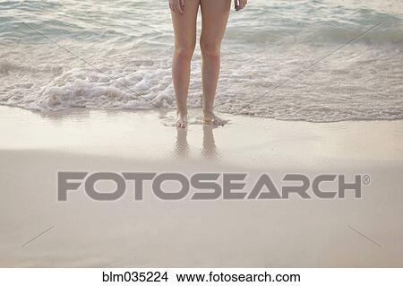 Picture - Caucasian girl standing in waves on beach. Fotosearch