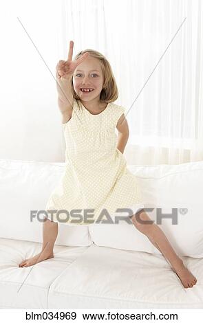 Caucasian girl standing on sofa gesturing peace sign View Large Photo Image Stock Photo - Caucasian girl standing on sofa gesturing peace sign. Fotosearch