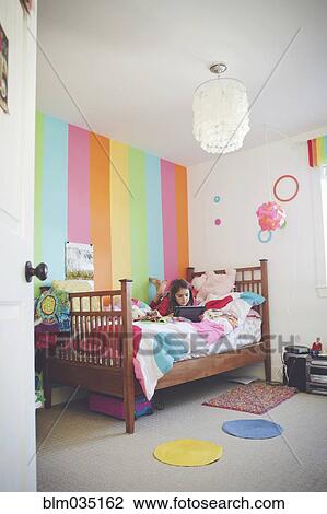 Stock Image - Caucasian girl using digital tablet in bedroom. Fotosearch