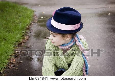 Stock Image - Caucasian girl wearing fedora hat on rainy concrete. Fotosearch