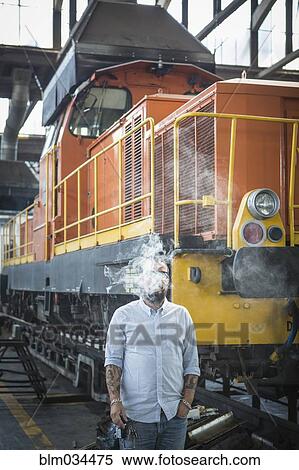 Caucasian man blowing smoke in train yard View Large Photo Image Stock Photography - Caucasian man blowing smoke in train yard. Fotosearch