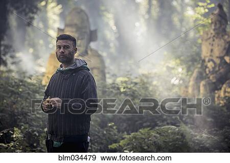 Stock Photo - Caucasian man exploring ancient statues in forest. Fotosearch