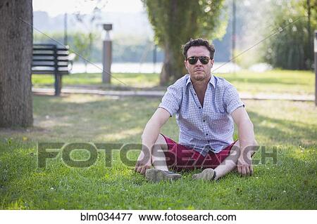 Caucasian man sitting in grass in park View Large Photo Image Stock Photo - Caucasian man sitting in grass in park. Fotosearch
