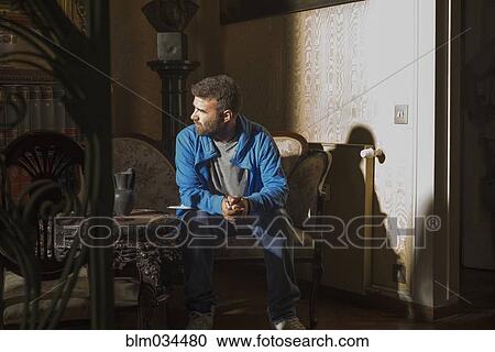 Stock Image - Caucasian man sitting in sunlight in living room. Fotosearch