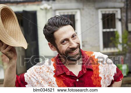Stock Image - Caucasian man tipping straw hat in backyard. Fotosearch