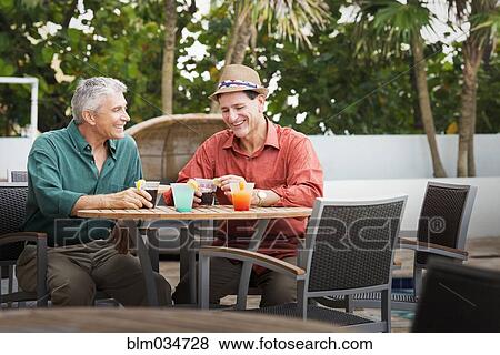 Stock Photo - Caucasian men with cocktails on restaurant patio. Fotosearch